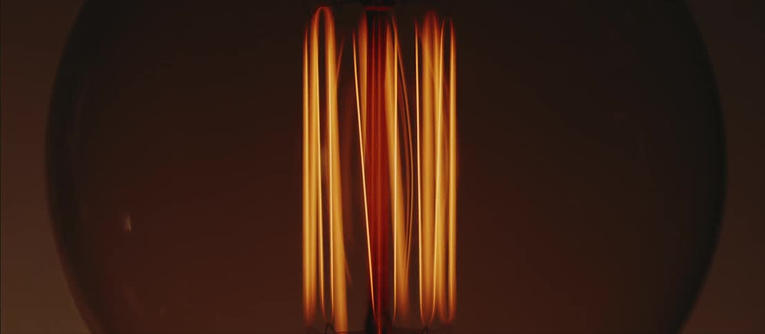 Yellow lamp bulb filaments turning on inside a dimly lit room