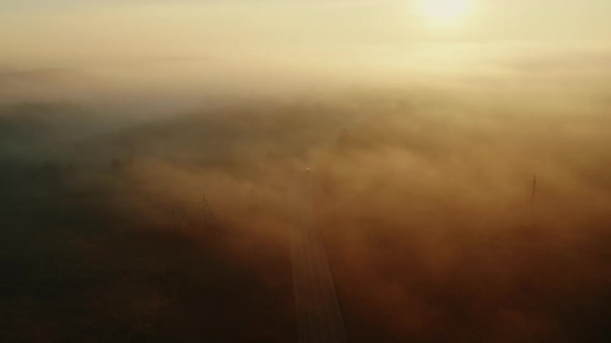 Aerial view of vehicle driving on road in the fog at sunset