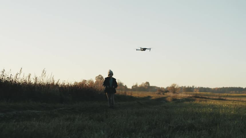 A young boy walks through a field and flies a toy airplane