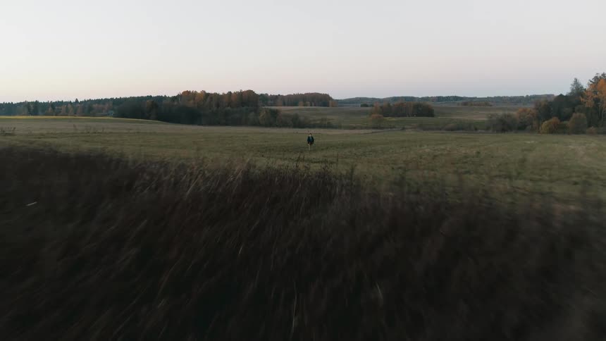 Boy standing in the middle of a field next to a dirt road flies a drone