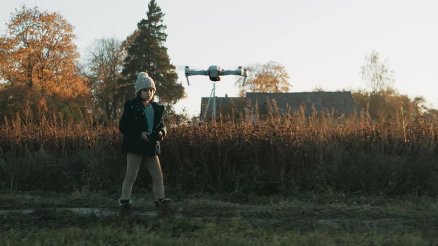 A child controls a flying drone in a rural field