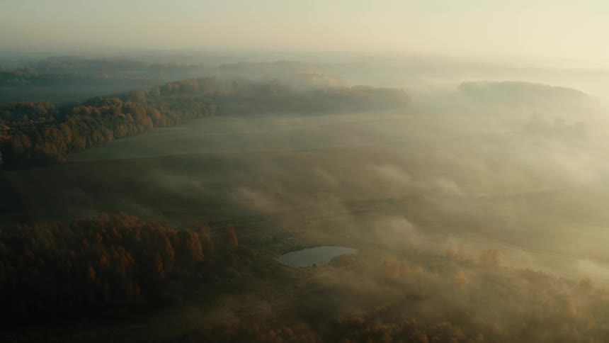 Heavy fog fills the air over a vast forest where a lake sits in the middle