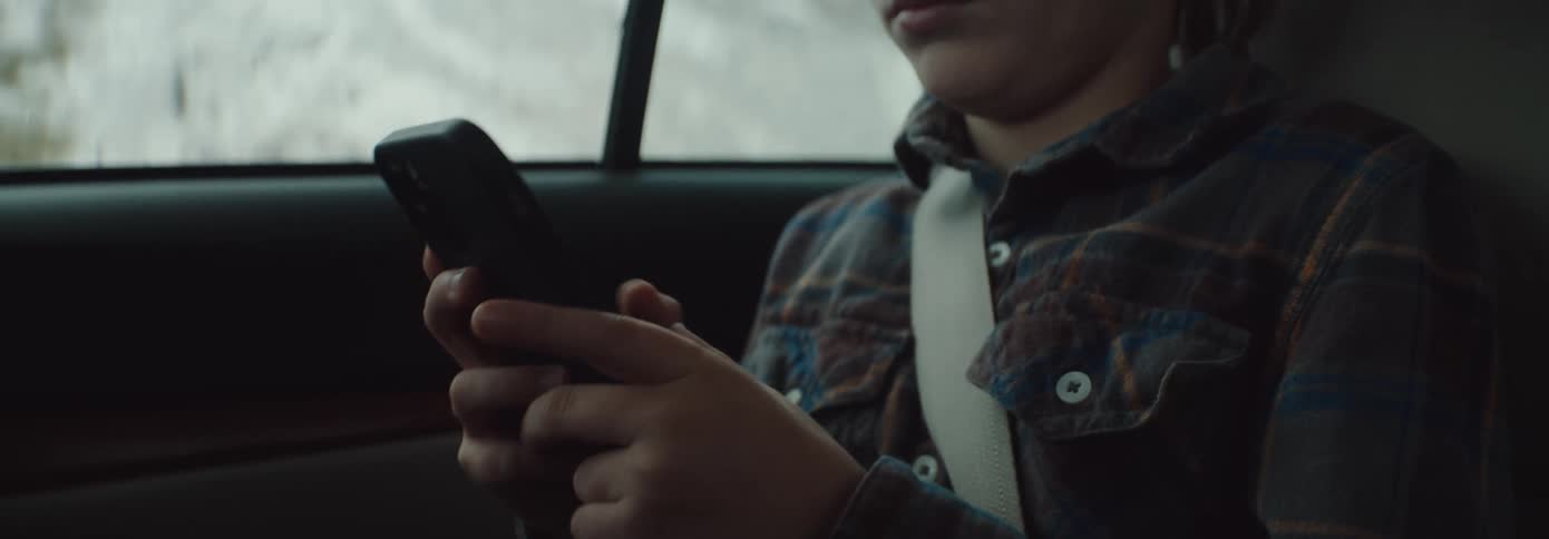 A young boy sits in a car and uses a cell phone