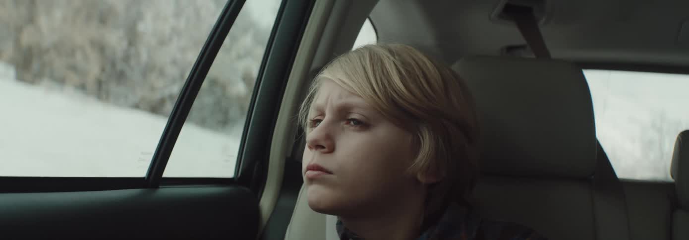 A young boy sits in a car and looks out the window during a drive