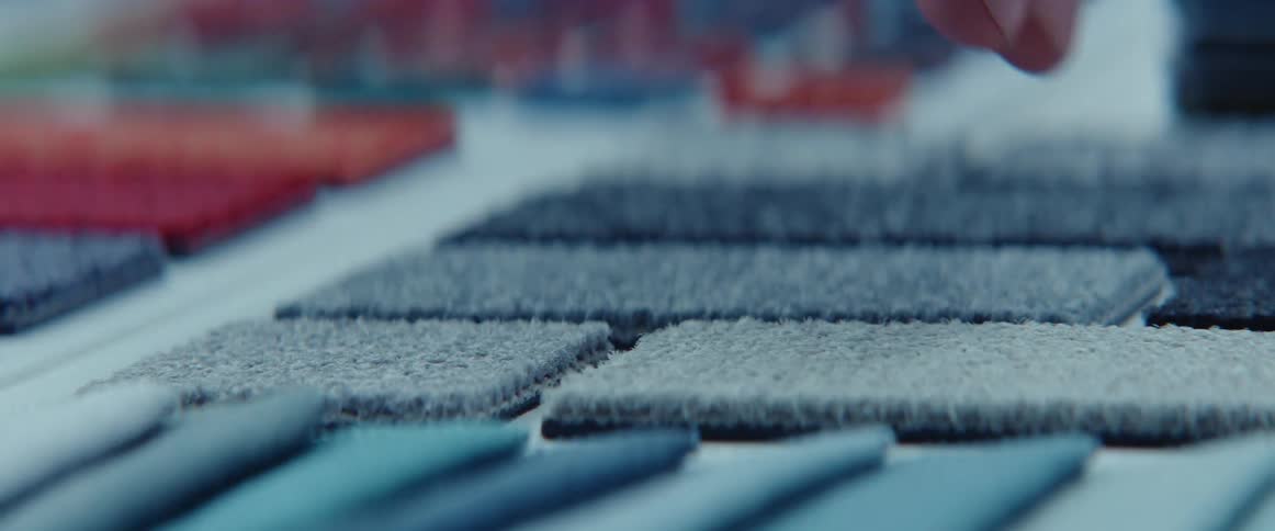 A person touches carpet samples on a table with their fingers