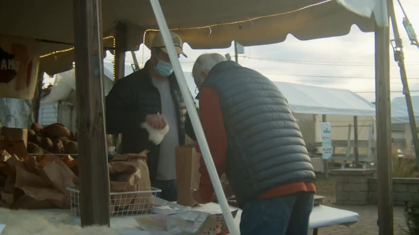 A man packing food into a bag for a customer at an outdoor tented market area