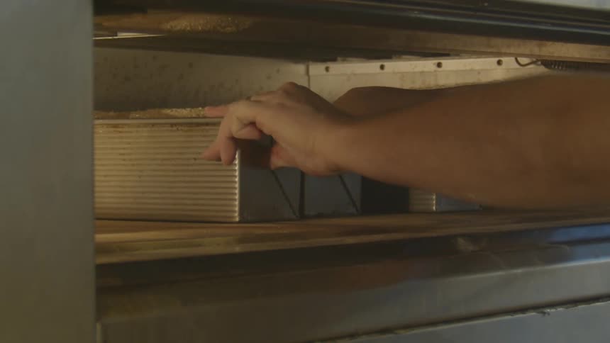 A person loading an oven with loafs of bread