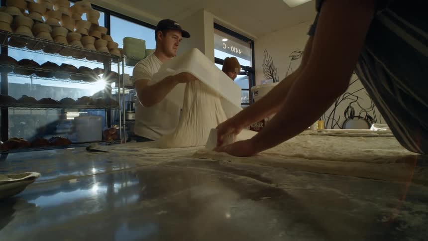 Some coworkers working at a bakery with dough