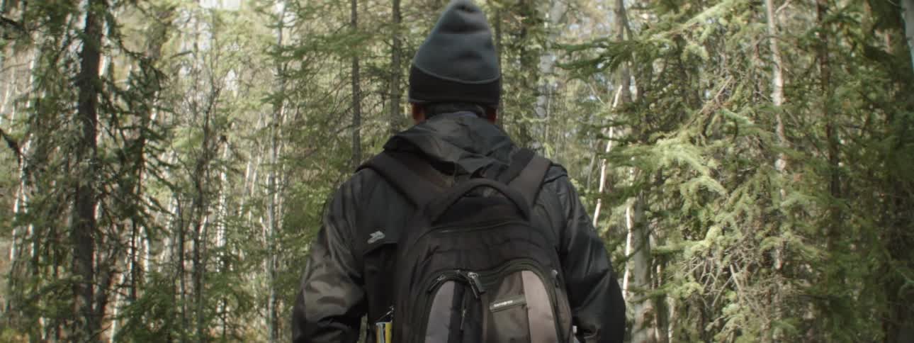 A man looks around as he hikes through a forest