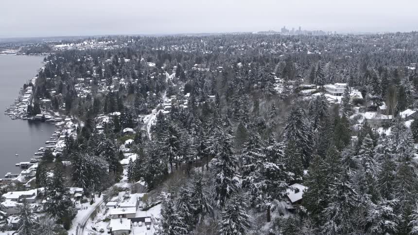 Flying low over a snowy hillside neighborhood with downtown Seattle in the distance