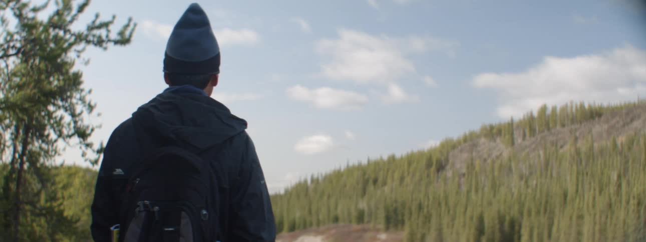 A man stands in a forest and looks down at the water