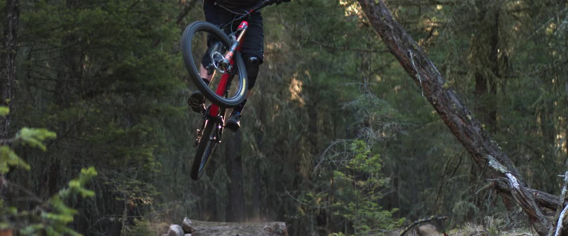 Mountain cyclist stylishly jumps in the air over gap on forest bike trail