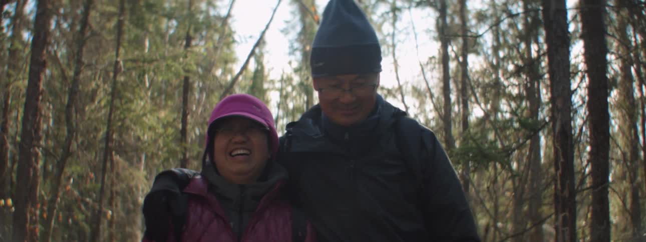 A man and woman hike together through a woodland in winter gear during the day