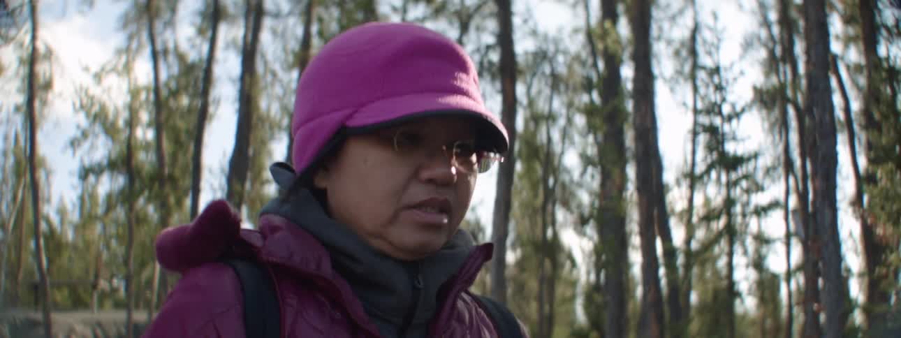Woman wearing cold weather gear walks away from others in forest