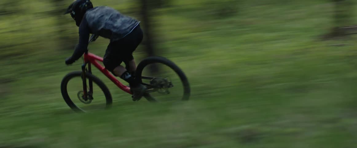 Cyclist rides a mountain bicycle on a dirt trail through the green forest meadow