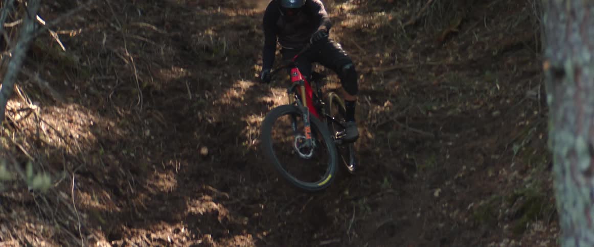 A man bikes down a hill in a forest and turns his bike sideways off a drop