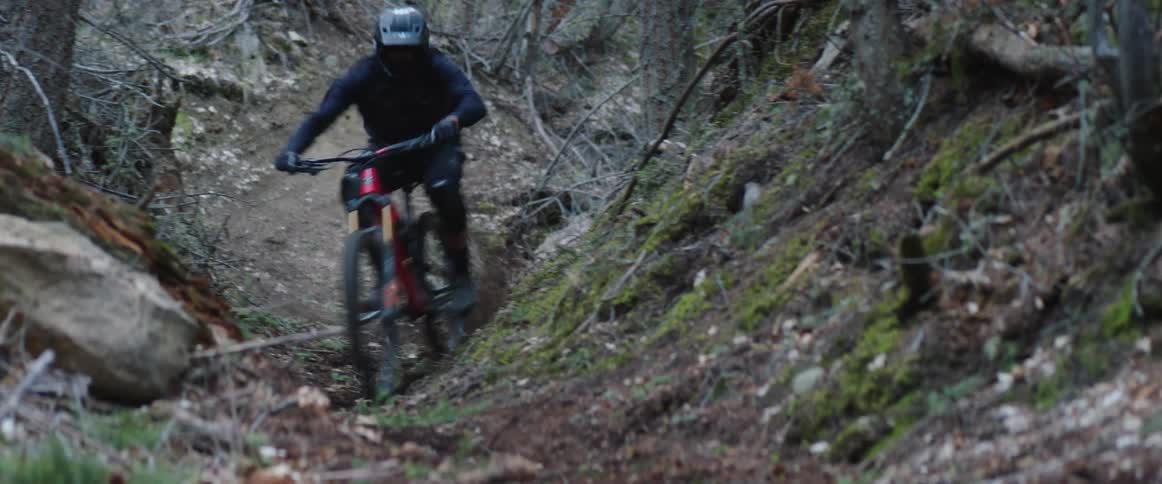 An athlete with a mountain bike riding a forest ravine trail at speed