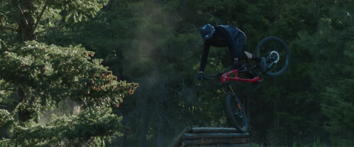Mountain bike athlete hits large dirt jump and stylishly whips bike sideways in the morning sunlight
