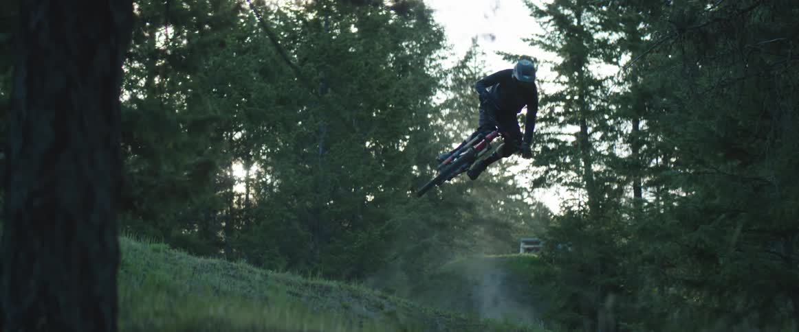 A cyclist jumps over a grass covered hill in a forest