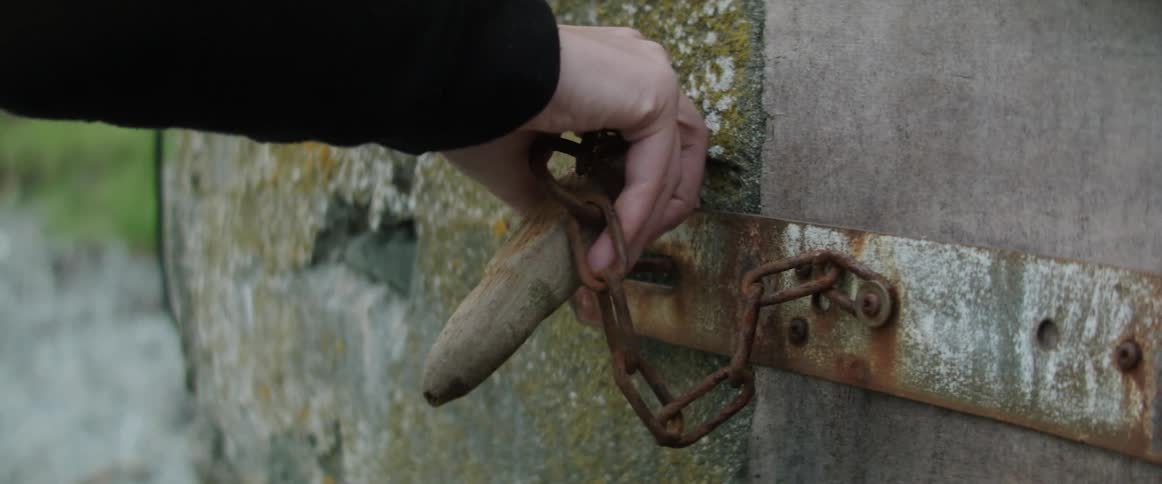 A hand lifts a chained peg from a gate lock and pulls the door open