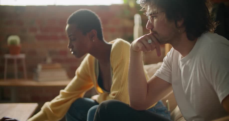 A man and woman sit on a couch and look at a computer
