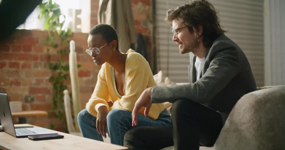 A man and woman watch a laptop together on the couch