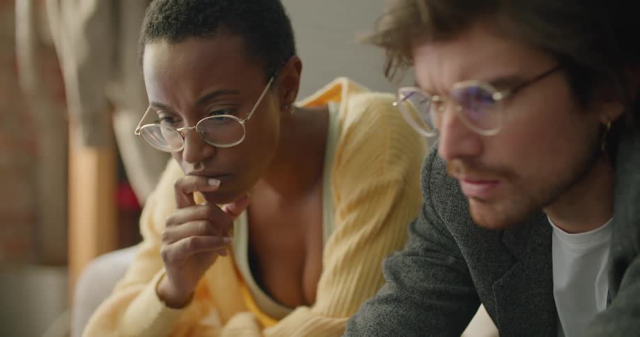 A man types on a laptop while sitting beside a woman on a sofa in house during the day