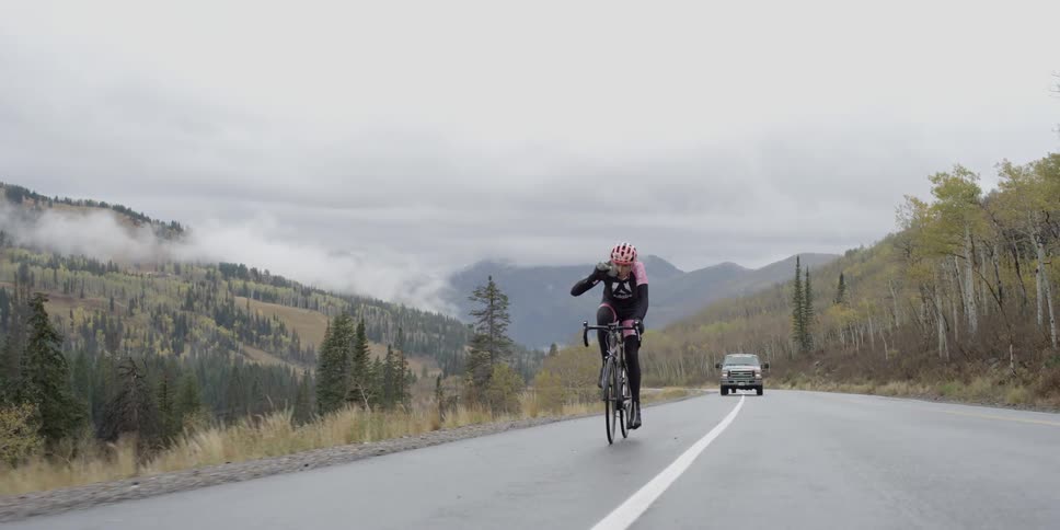 A bicyclist rides in the breakdown lane of a road and has a vehicle trailing him