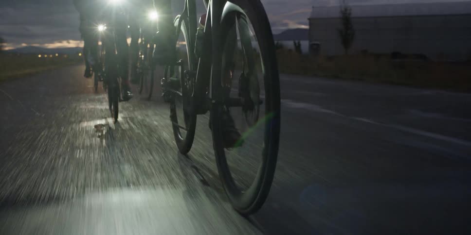 Three people riding bicycles down a road at dusk