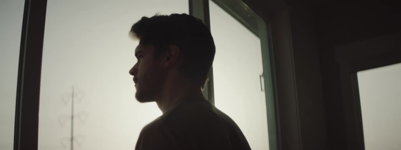 Man with a beard looks out the window and is silhouetted against the shining sun