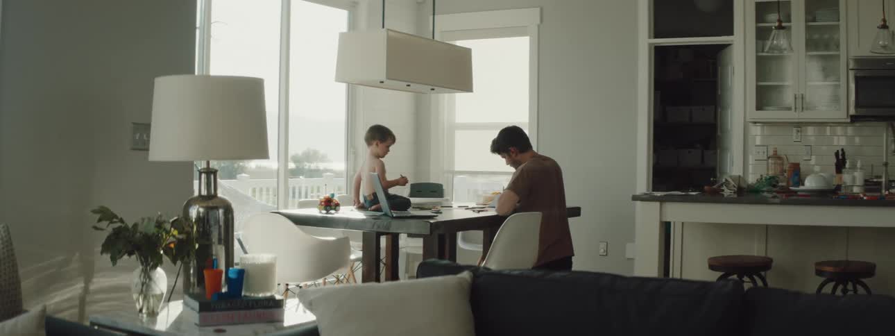 A father is working while his son sits at the table
