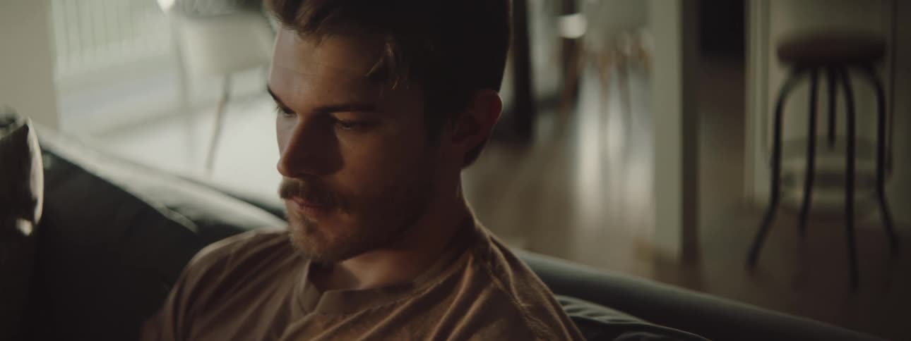 A man sitting alone on a couch at home with a sad contemplative expression on his face
