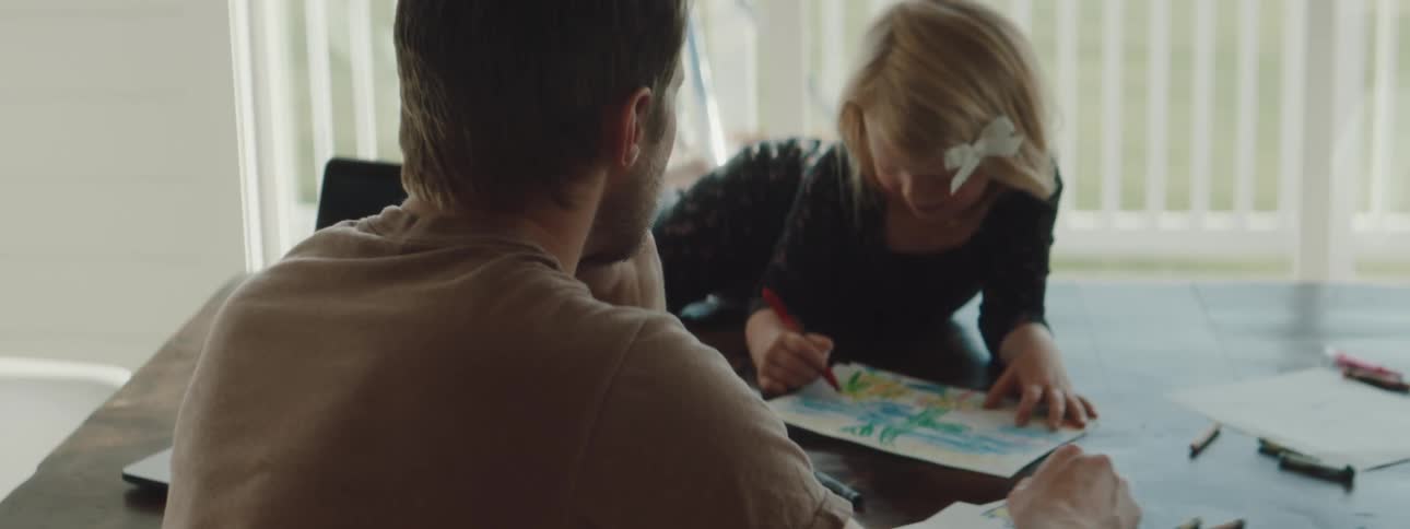 A man and young girl sit at a table and color together
