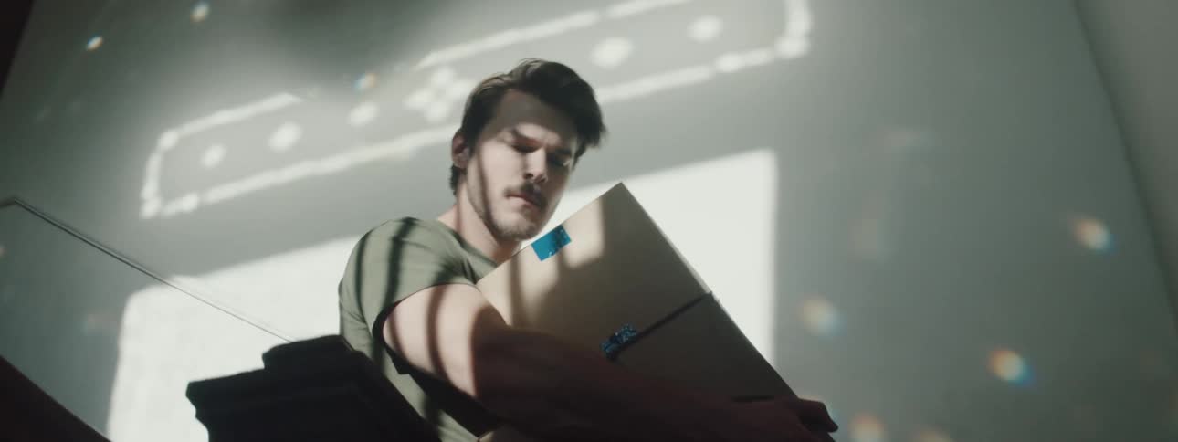 Man with a beard and a t shirt carries boxes and goes downstairs