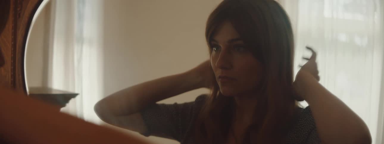 A woman is brushing her hair and looking into a mirror