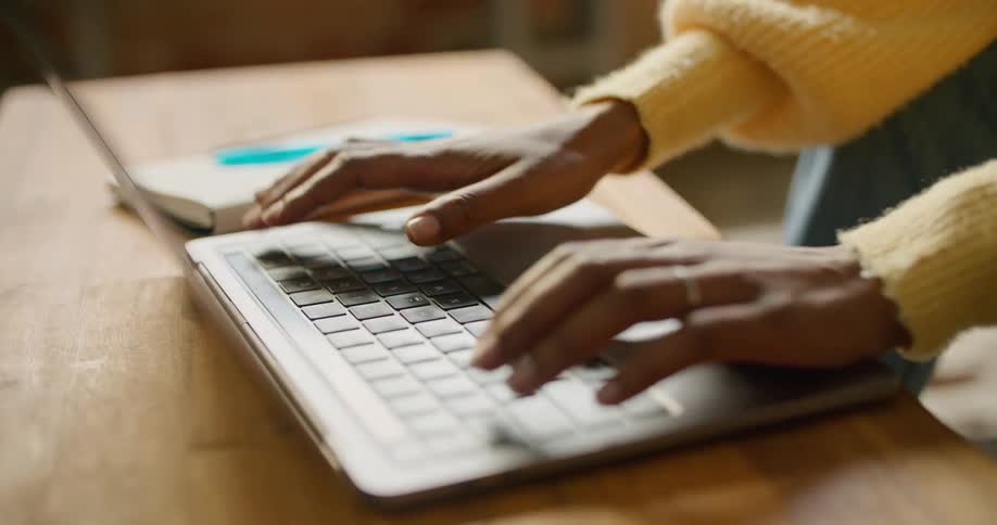 A woman is sitting in a room and typing on a laptop