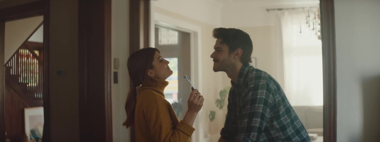 Man kisses his wife in the mouth while she brushes her teeth