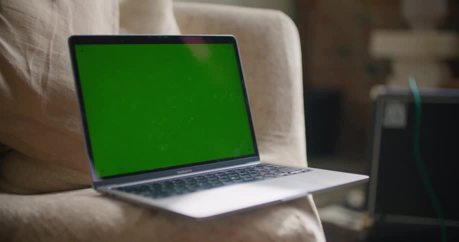 Laptop with a replaceable green screen sitting over couch