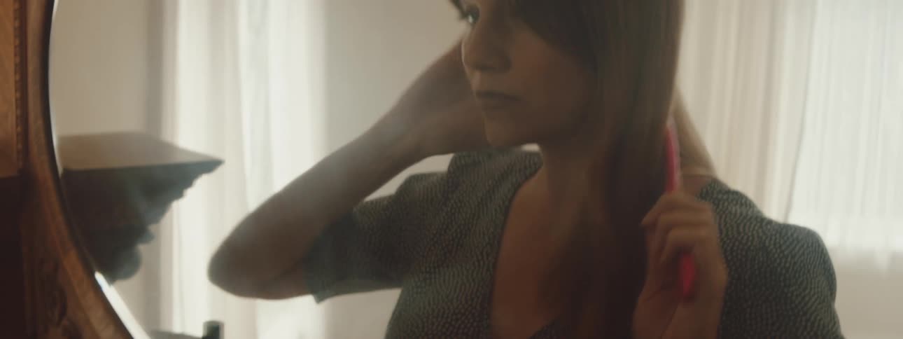 A woman is looking in a mirror and brushing her hair