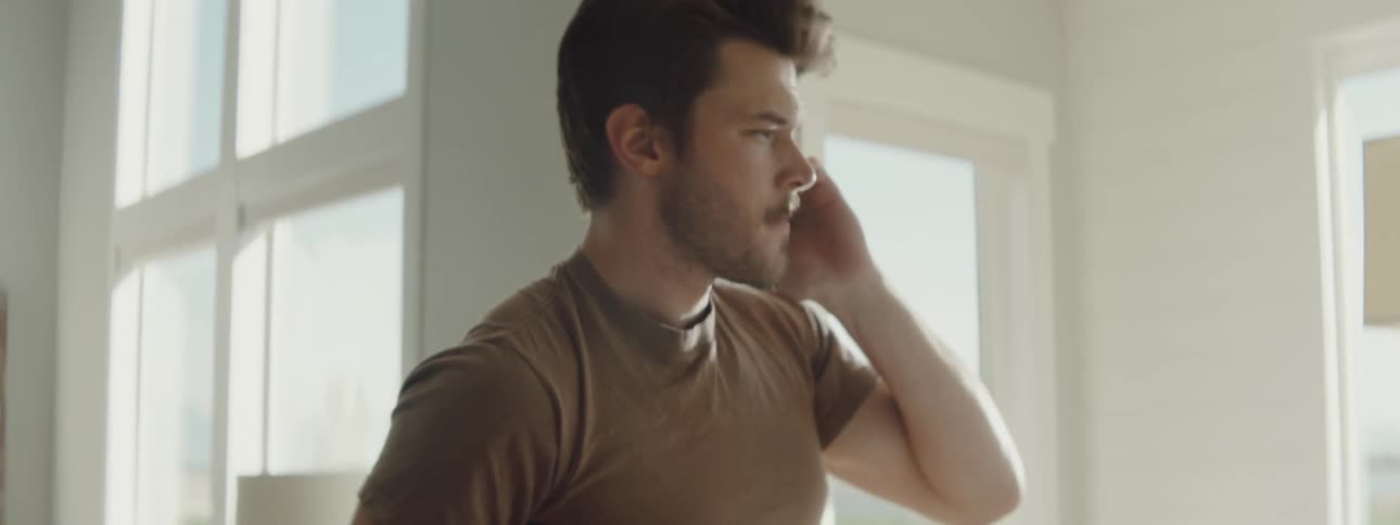 A man at home talks on his cell phone takes a bite of toast and looks at his laptop