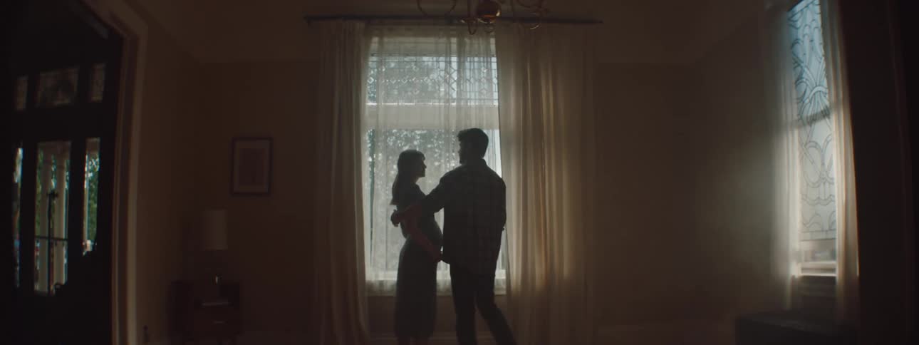 Man walks towards a woman and they embrace while standing in front of a window