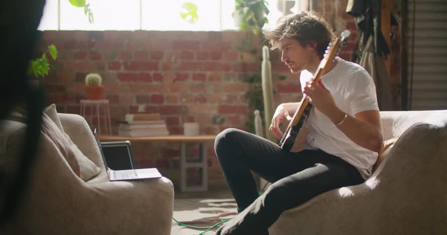 A man is sitting indoors and playing guitar