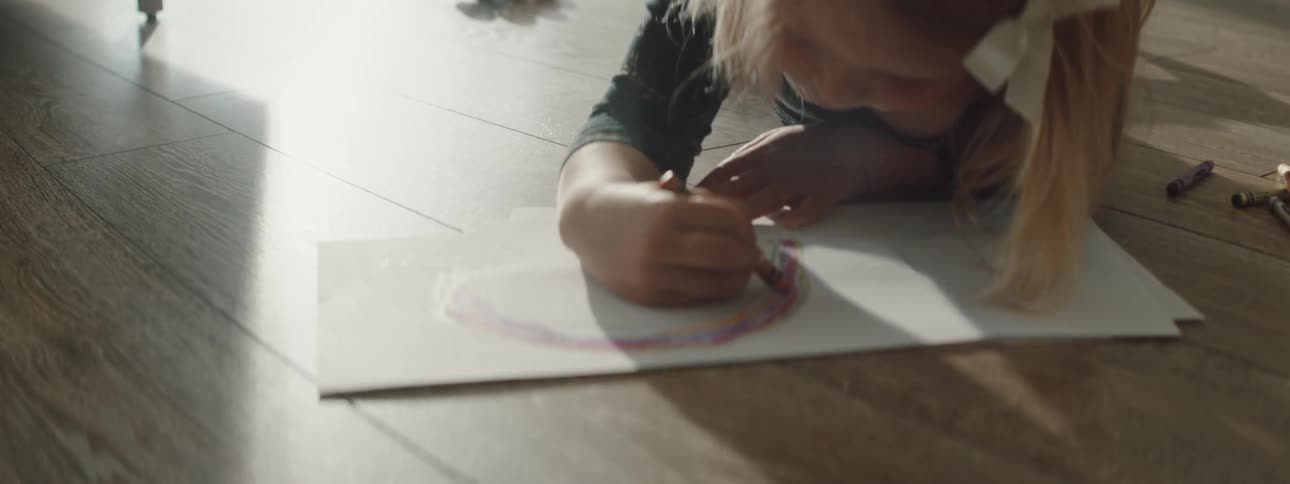 A child is coloring on some paper on the ground
