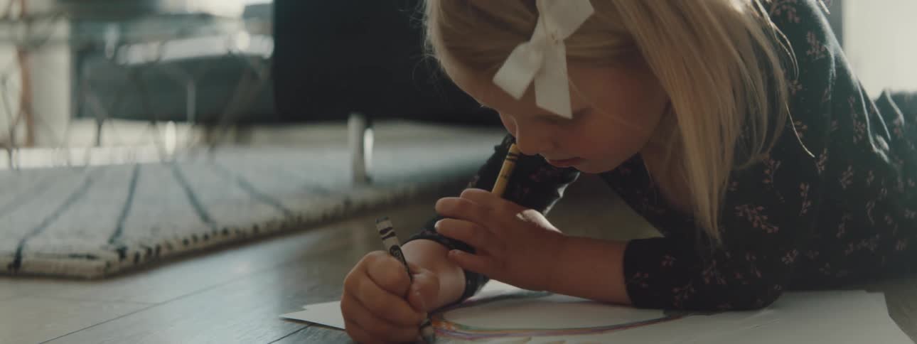 Girl drawing with crayons on the floor fo the living room