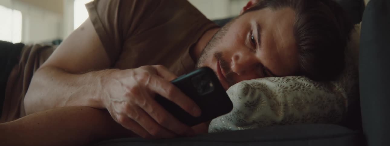 A man is using his phone while laying on the couch