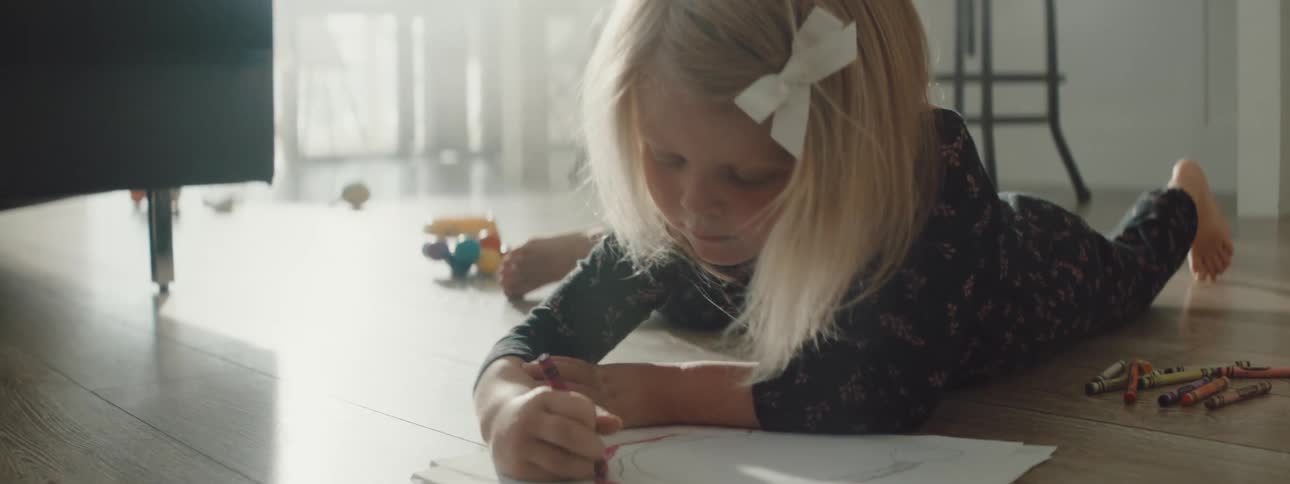 A girl colors on the floor in the living room