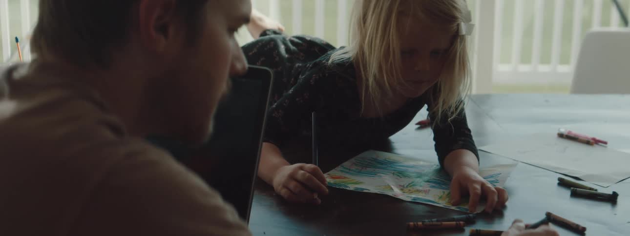 A man and a girl coloring with crayons on papers on a table
