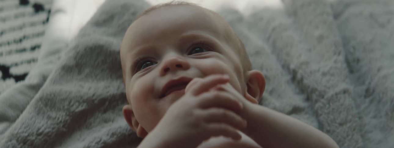 Baby clasps its hands near its mouth while laying on a blanket