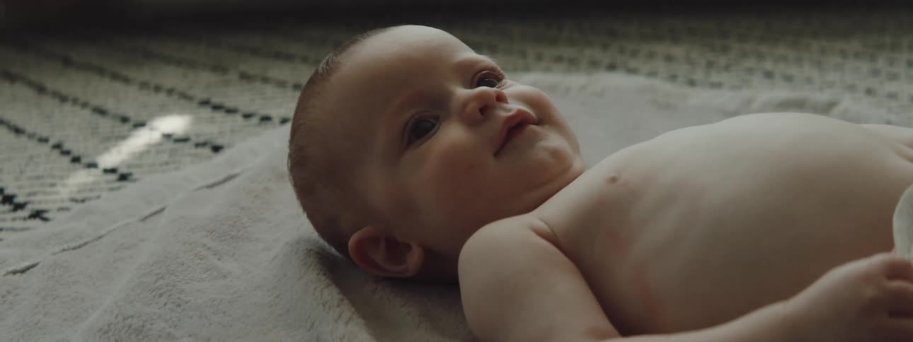 A baby is laying on a blanket moving its arms around and smiling