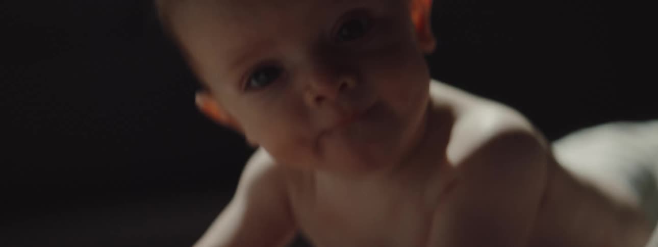 A baby with diapers in a room crawling on the floor with a wall in the background